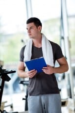 trainer with clipboard standing in a bright gym