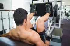 Rear view of male weightlifter doing leg presses in gym