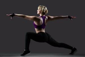 Beautiful dancer girl in sportswear doing lunge exercises with stretched arms, balance practice, on black background low key studio shot, side view