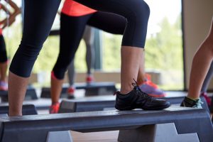 fitness, sport, people, step aerobics and lifestyle concept - close up of women legs exercising with steppers in gym