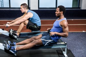Muscular men using rowing machine at gym