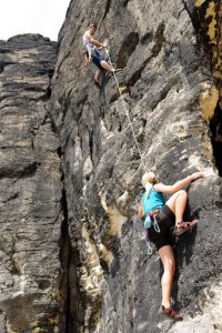 Rock climbing male instructor hold rope blond woman hanging