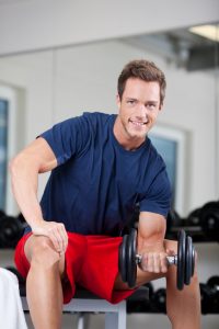 Happy muscular young man lifting weights in the gym