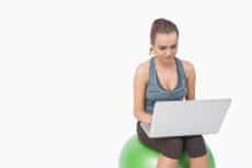 Young woman working with her laptop sitting on balance ball