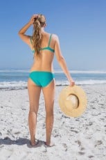 Rear view of fit woman in bikini on beach holding sunhat on a sunny day
