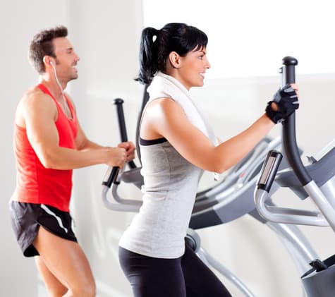 man and woman with elliptical cross trainer at gym