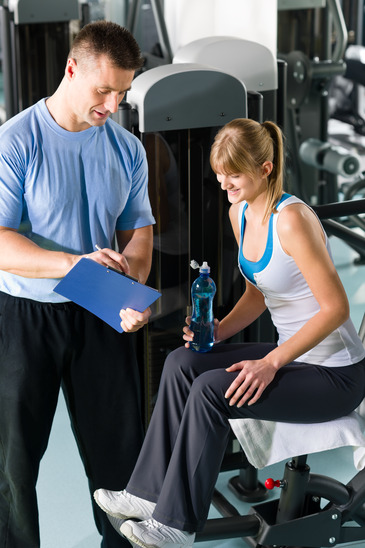 Personal trainer with young woman at gym