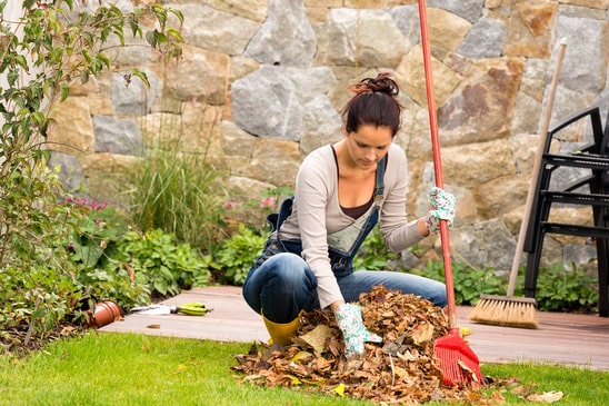 Young woman raking leaves autumn pile veranda