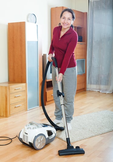 Happy mature woman vacuuming with vacuum cleaner