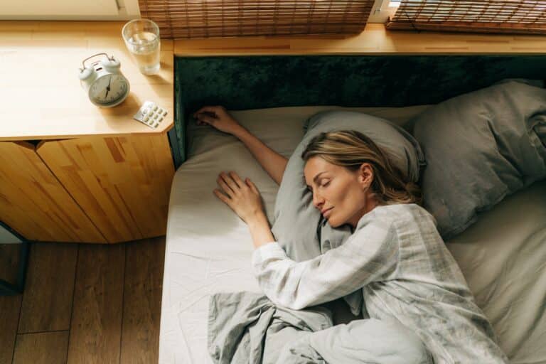 Top view of a sleeping woman. Clock and pills on the nightstand next to the bed.